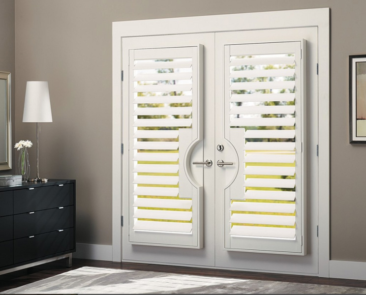 The image shows a large window with shutters partially open, allowing natural light to enter the room.