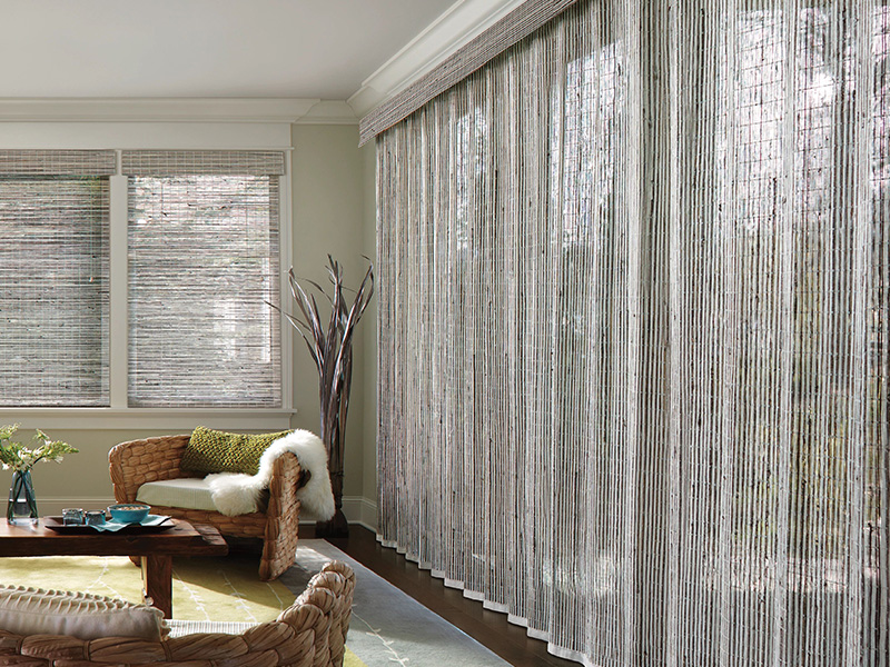 A room with a large window featuring metallic-looking vertical blinds, a woven area rug, and decorative elements.