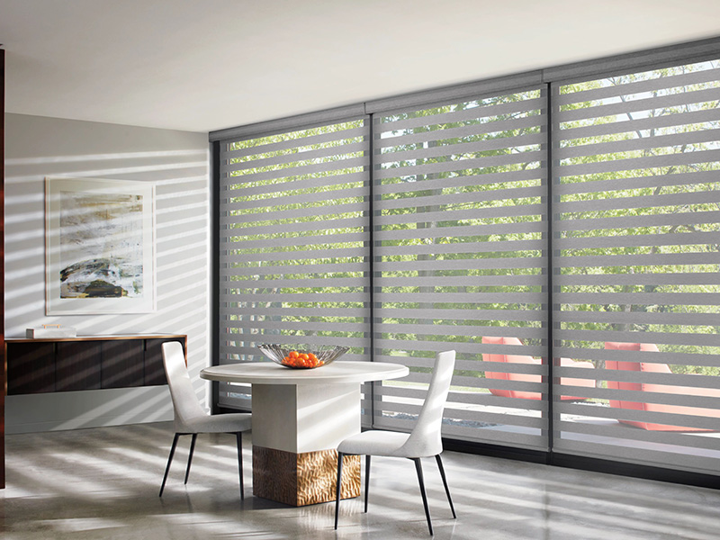 A modern interior with sliding glass doors and vertical blinds, featuring a dining table and chairs in a room illuminated by natural light.